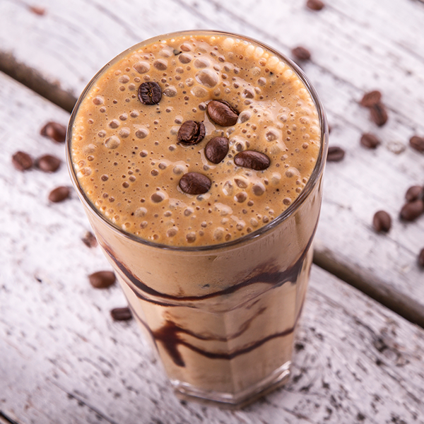 Bicchiere di vetro con frappè al caffè guarnito con chicchi di caffè su tavolo di legno