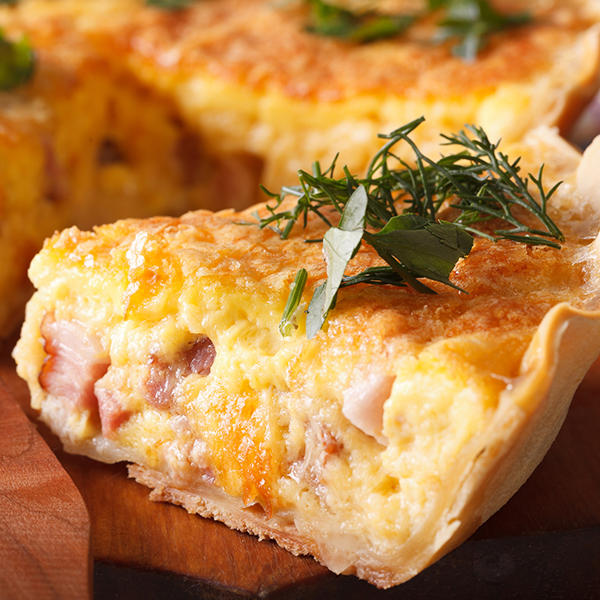 Fetta di quiche su tavola di legno guarnita con foglie di alloro e rametto di rosmarino