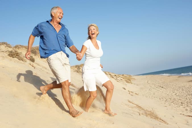 Uomo e donna di mezza età che corrono sorridenti sulla sabbia in riva al mare